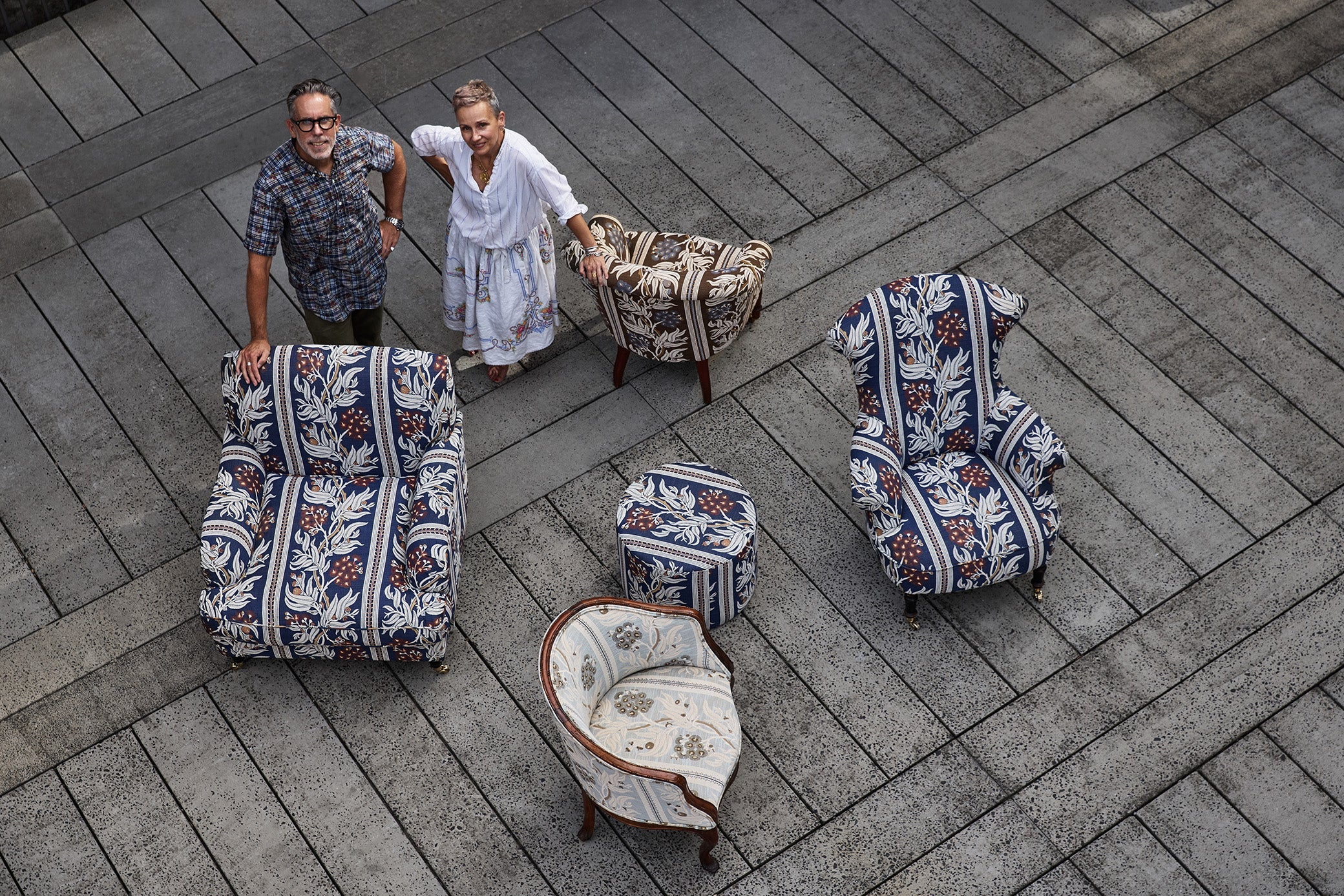 Overhead image of a couple standing among upholstered chairs on a wooden deck