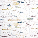 Detail of fabric in a painterly tree branch print in shades of brown, yellow and blue on a white field.