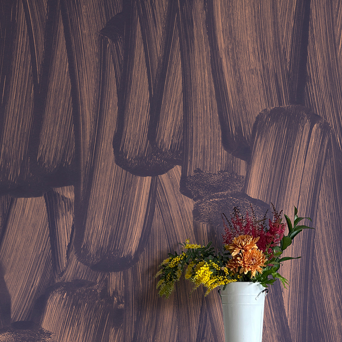 A vase of flowers stands in front of a wall papered in an abstract paint print in dark grey on a purple field.