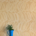 A vase of flowers stands in front of a wall papered in a playful paint print in cream on a tan field.