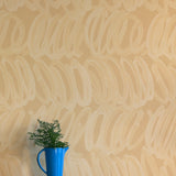 A vase of flowers stands in front of a wall papered in a playful paint print in cream on a tan field.