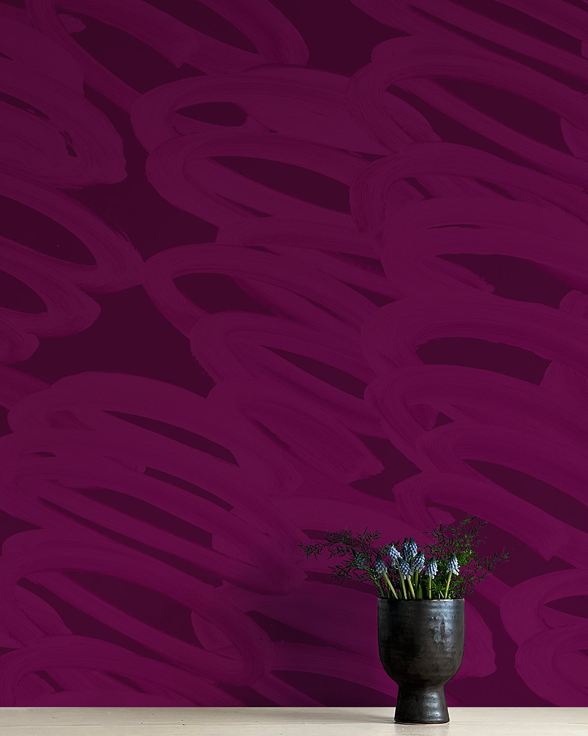 A vase of flowers stands in front of a wall covered in an abstract paintstroke print in magenta on a dark purple field.
