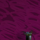 A vase of flowers stands in front of a wall covered in an abstract paintstroke print in magenta on a dark purple field.