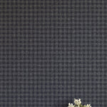A vase of flowers stands in front of a wall papered in a dense plaid pattern in shades of navy.