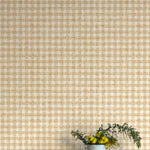 A vase of flowers stands in front of a wall papered in a dense plaid pattern in shades of orange and tan.