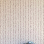 A vase of flowers stands in front of a wall covered in a repeating striped circular print in purple on a cream field.