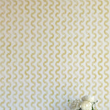 A vase of flowers stands in front of a wall papered in a playful curvy stripe print in yellow on a cream field.