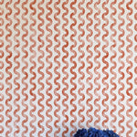 A vase of flowers stands in front of a wall papered in a playful curvy stripe print in red on a cream field.