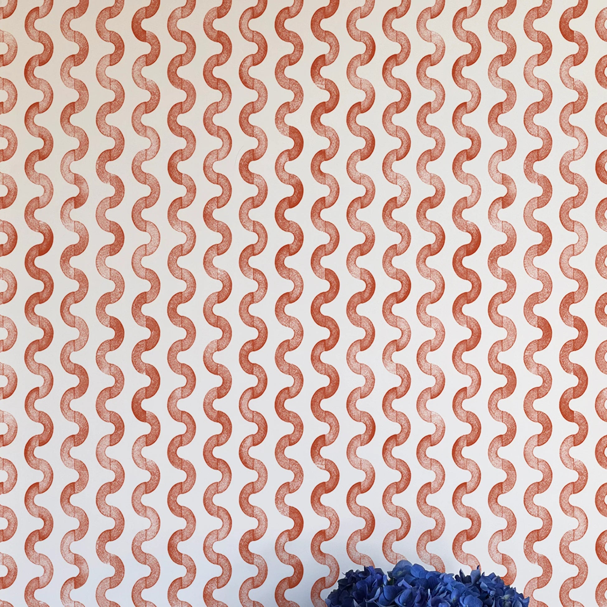 A vase of flowers stands in front of a wall papered in a playful curvy stripe print in red on a cream field.