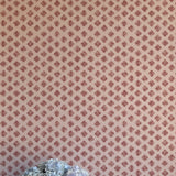 A vase of flowers stands in front of a wall covered in a minimalist quatrefoil pattern in red on a cream field.