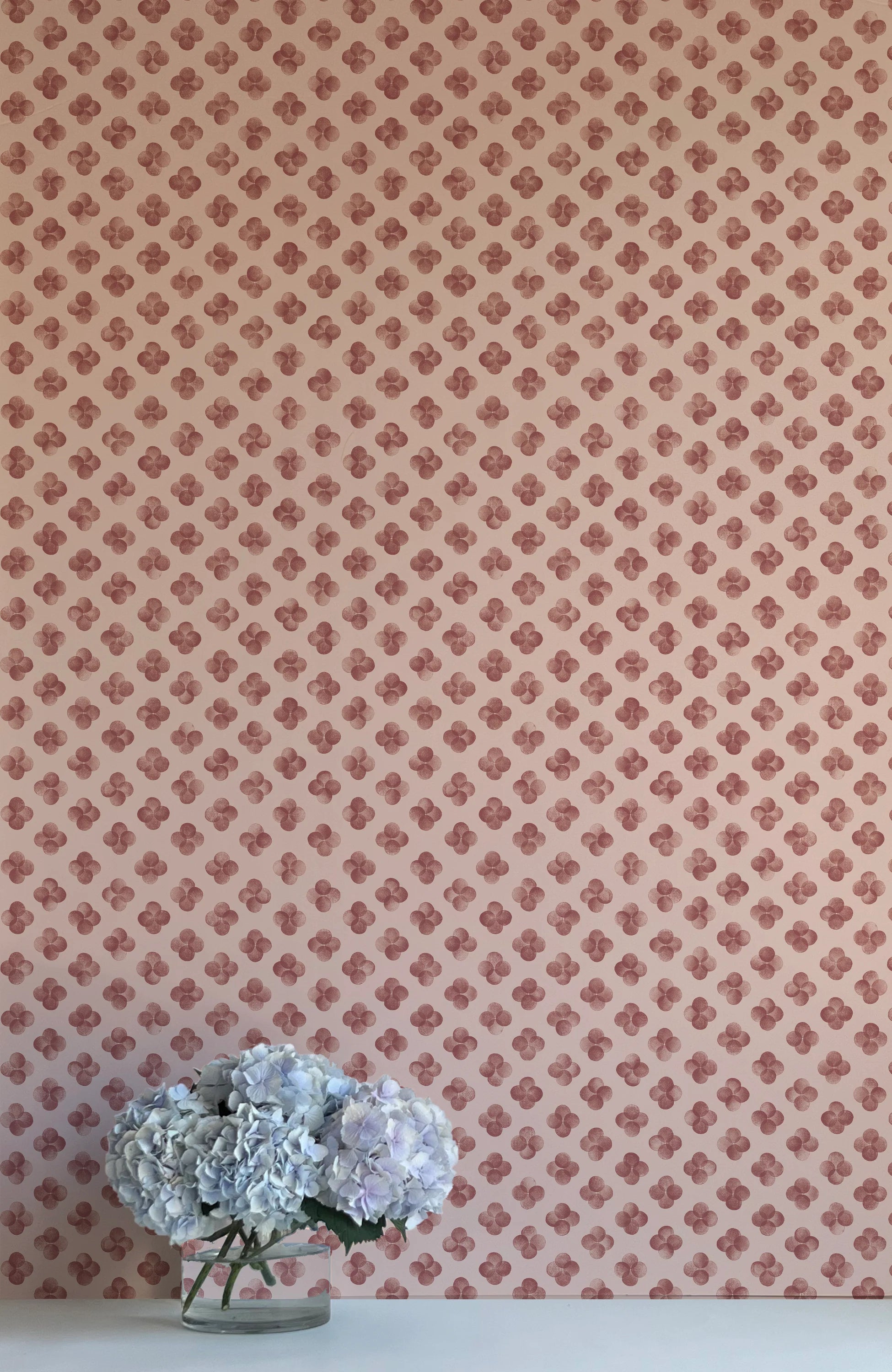 A vase of flowers stands in front of a wall covered in a minimalist quatrefoil pattern in red on a cream field.