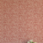 A vase of flowers stands in front of a wall covered in a textural grid print in shades of red and cream.