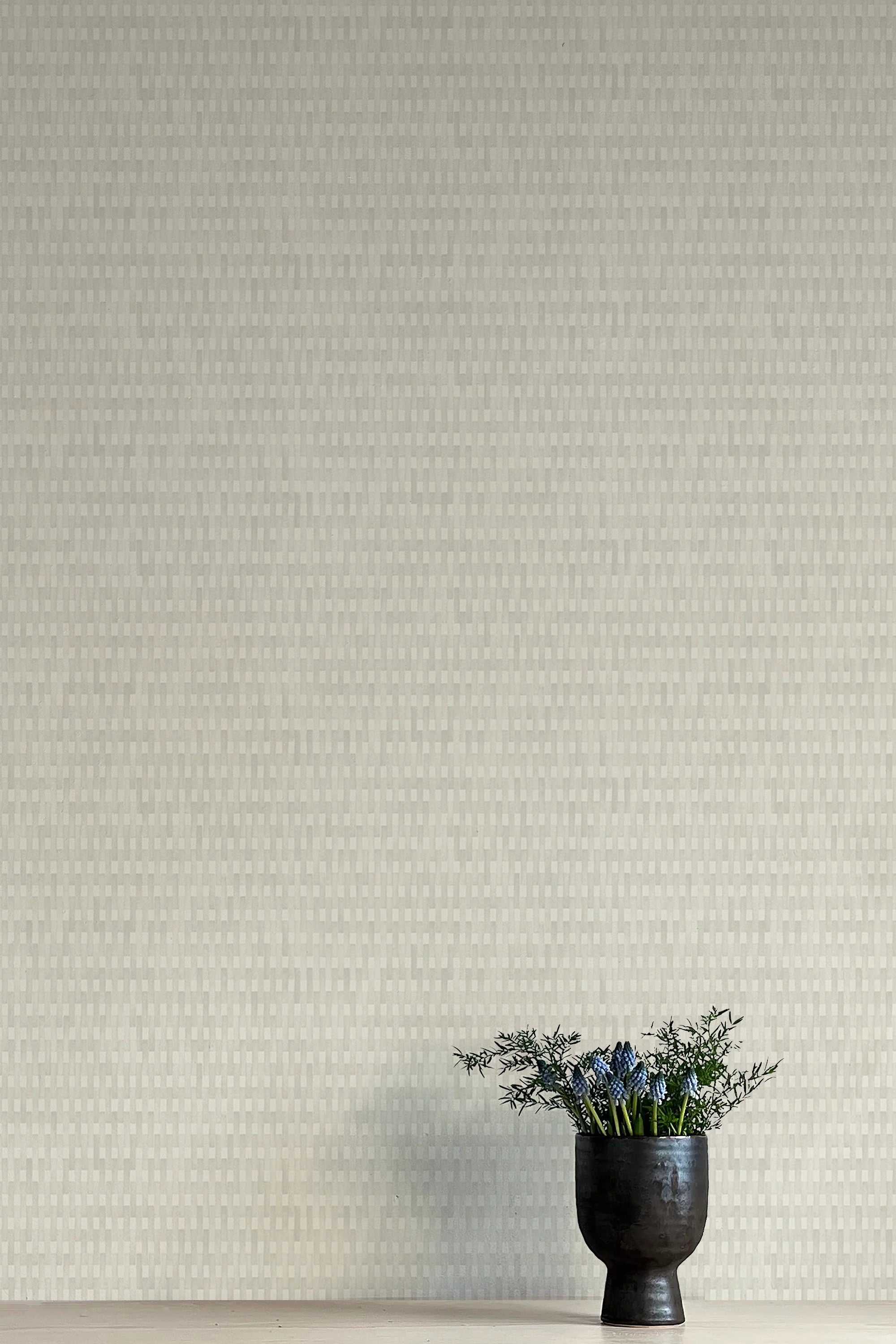 A vase of flowers stands in front of a wall covered in a textural grid print in shades of gray.