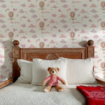 Bedroom with wooden headboard, white pillows, teddy bear, and hot air balloon wallpaper.