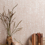 Mantle vignette with vase and brances and antique books in front of a wall papered in a painterly dashed dot print in white on a pale pink field.