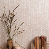 Mantle vignette with vase and brances and antique books in front of a wall papered in a painterly dashed dot print in white on a pale pink field.