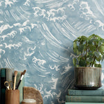 Mantle vignette with antique books, potted plant and pencil jar against wallpaper  in a playful wave print in white on a chambray blue field.