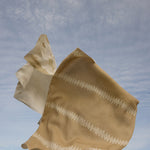 Beige fabric with white patterns blowing in the wind against a blue sky.