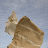 Beige fabric with white patterns blowing in the wind against a blue sky.
