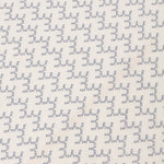 Detail of embroidered fabric in a linear geometric print in white and navy on a cream field.