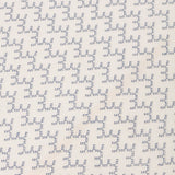 Detail of embroidered fabric in a linear geometric print in white and navy on a cream field.