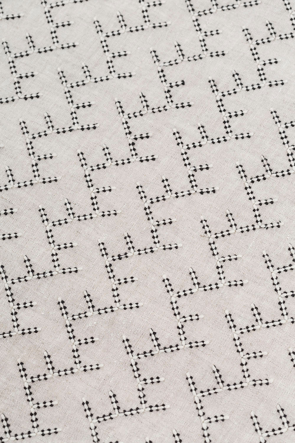 Detail of embroidered fabric in a linear geometric print in white and black on a cream field.