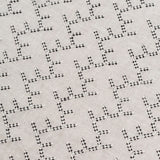Detail of embroidered fabric in a linear geometric print in white and black on a cream field.