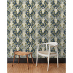Chair and stool in front of a wall papered in a large, painterly vase and leaf print over a repeating diamond background in shades of blue.