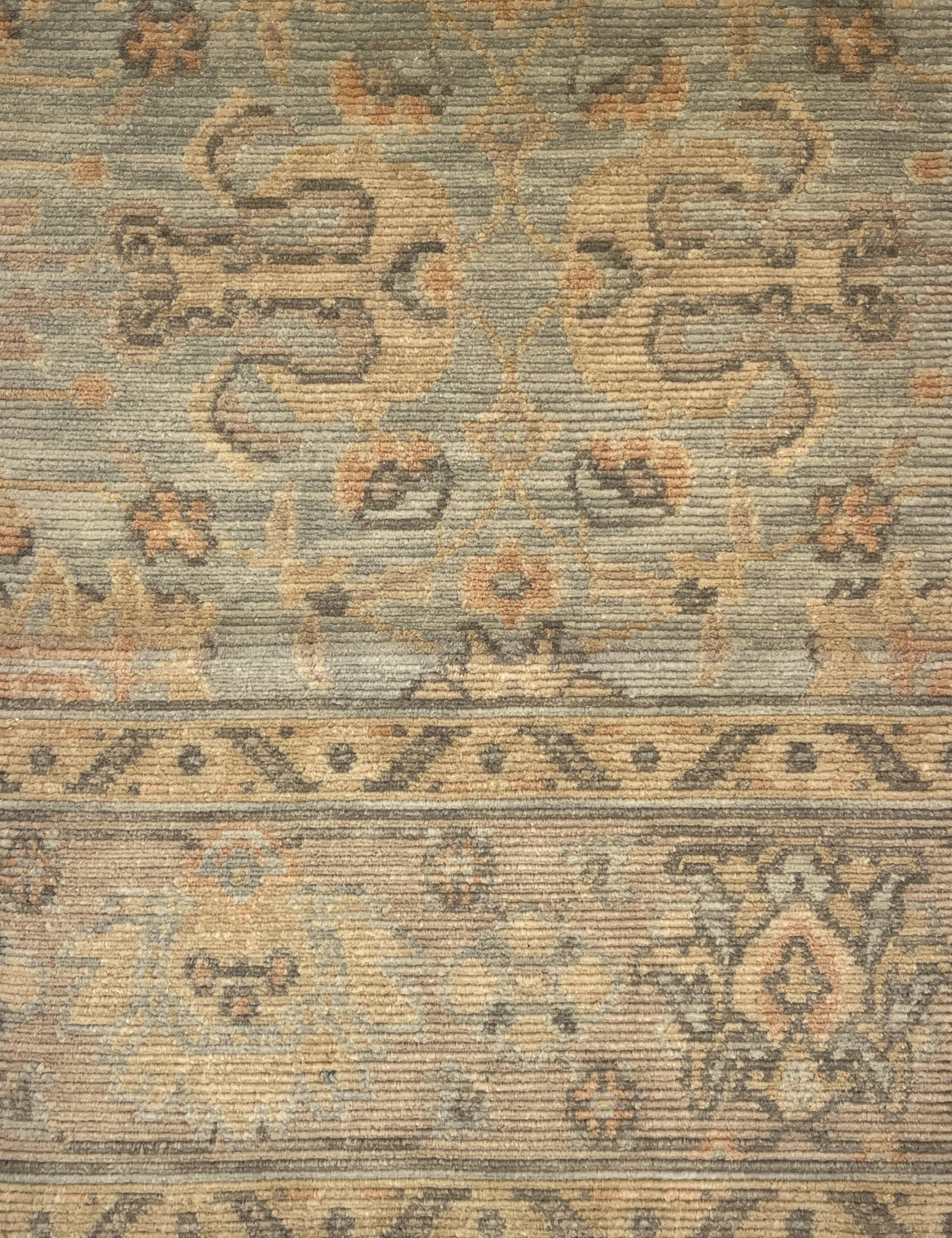 A close-up of a vintage-style area rug with a distressed, low-pile texture. The design features muted beige, gray, and brown tones with traditional floral and geometric motifs.