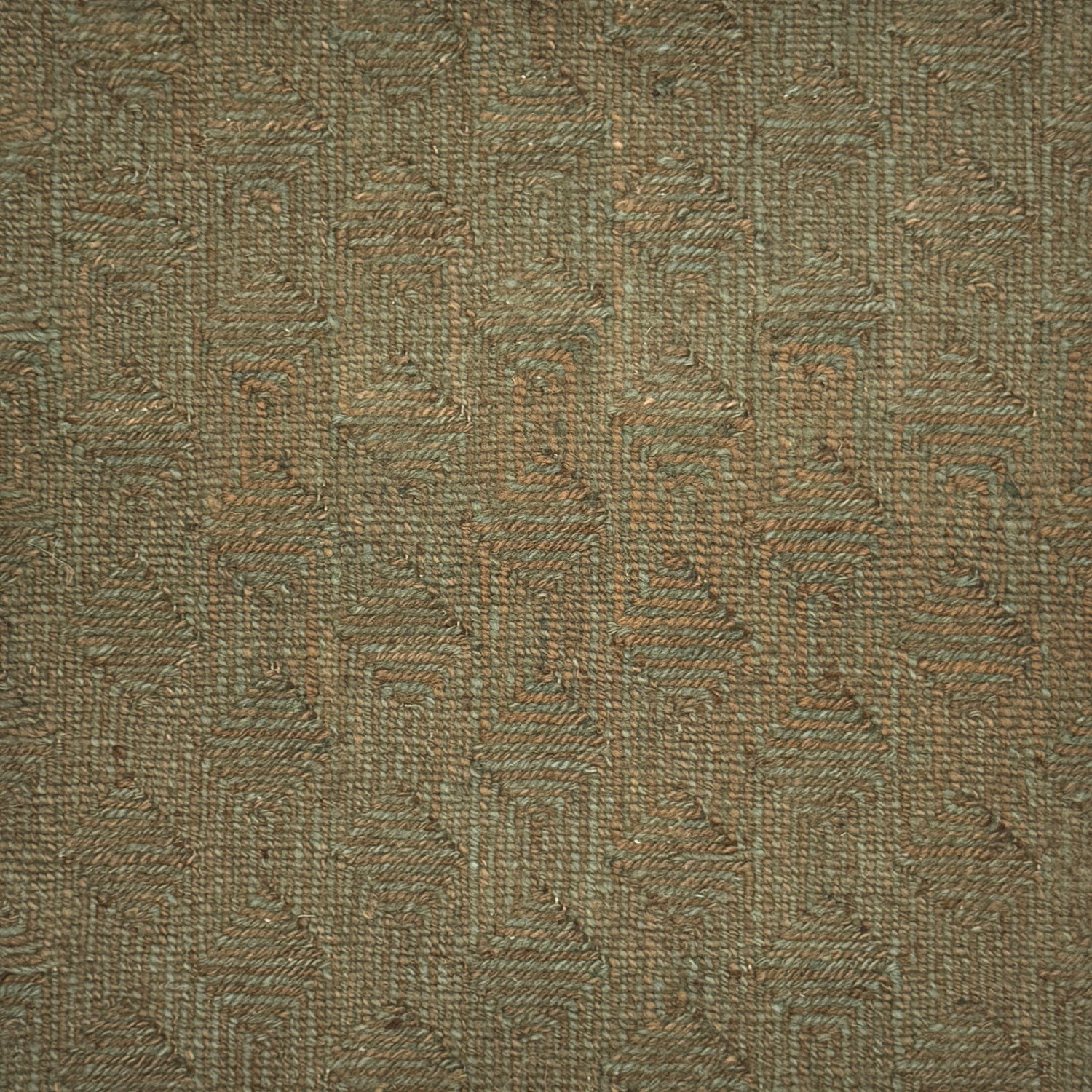 A close-up of flatweave rug  with a repeating geometric pattern in dark brown and sage green. 