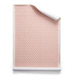 Roll of wallpaper with small scale playful geometric lattice pattern in pink and white on a white background.