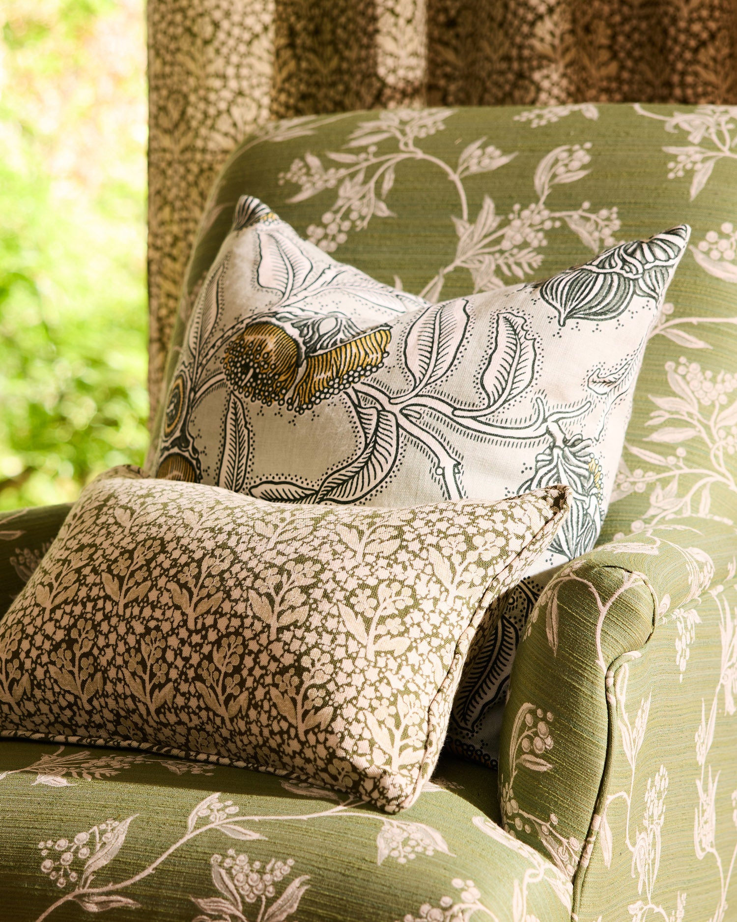 Decorative pillows with floral patterns on a green upholstered chair.