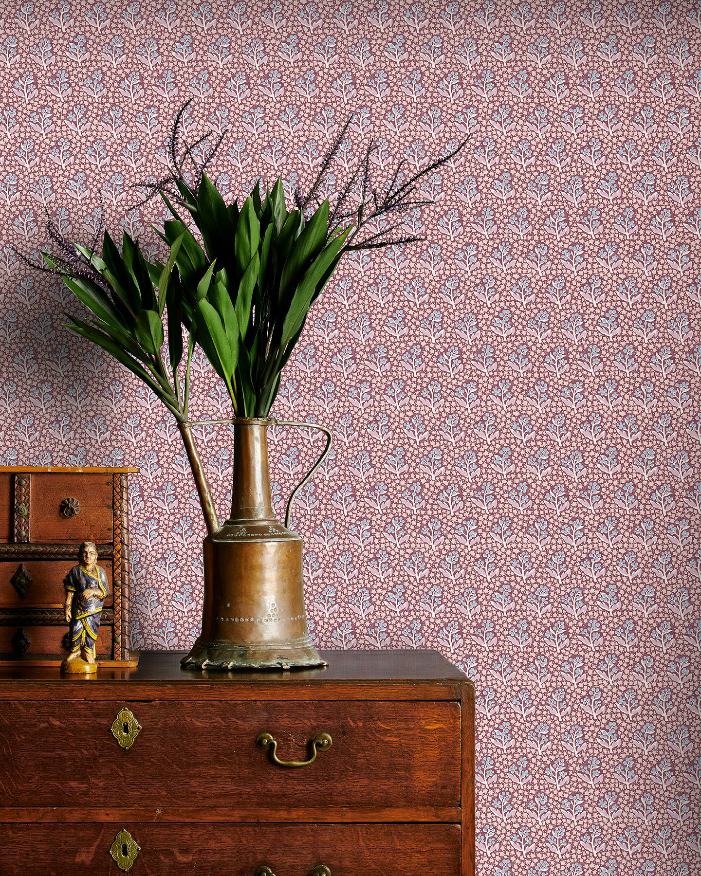 Vintage-style wallpaper with intricate patterns, a brass vase with greenery on a wooden dresser.