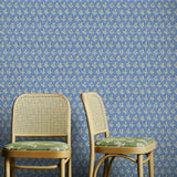 Two wicker chairs with green cushions against a blue floral wallpapered wall.