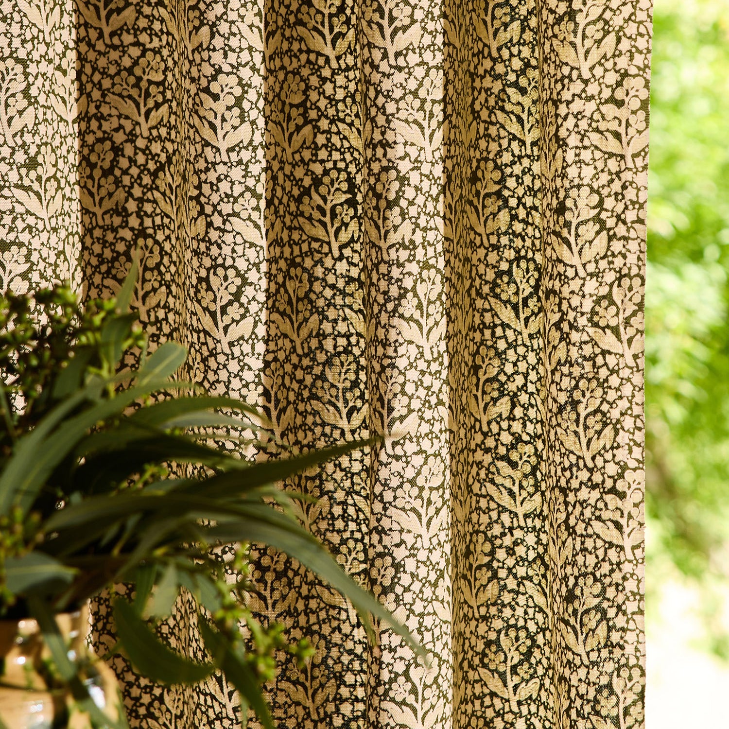 Vase with greenery on a wooden table against a a green floral patterned curtain