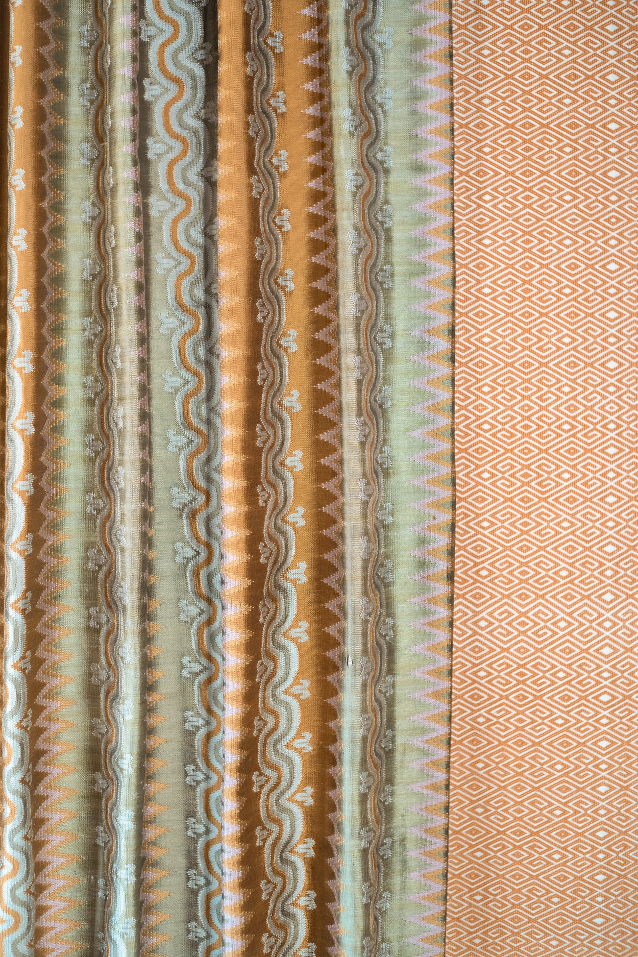 Patterned fabric with vertical stripes and geometric designs in brown, green, and beige.