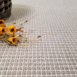 Carpet in a taupe plaid pattern with a small arrangement of yellow flowers and dried elements.