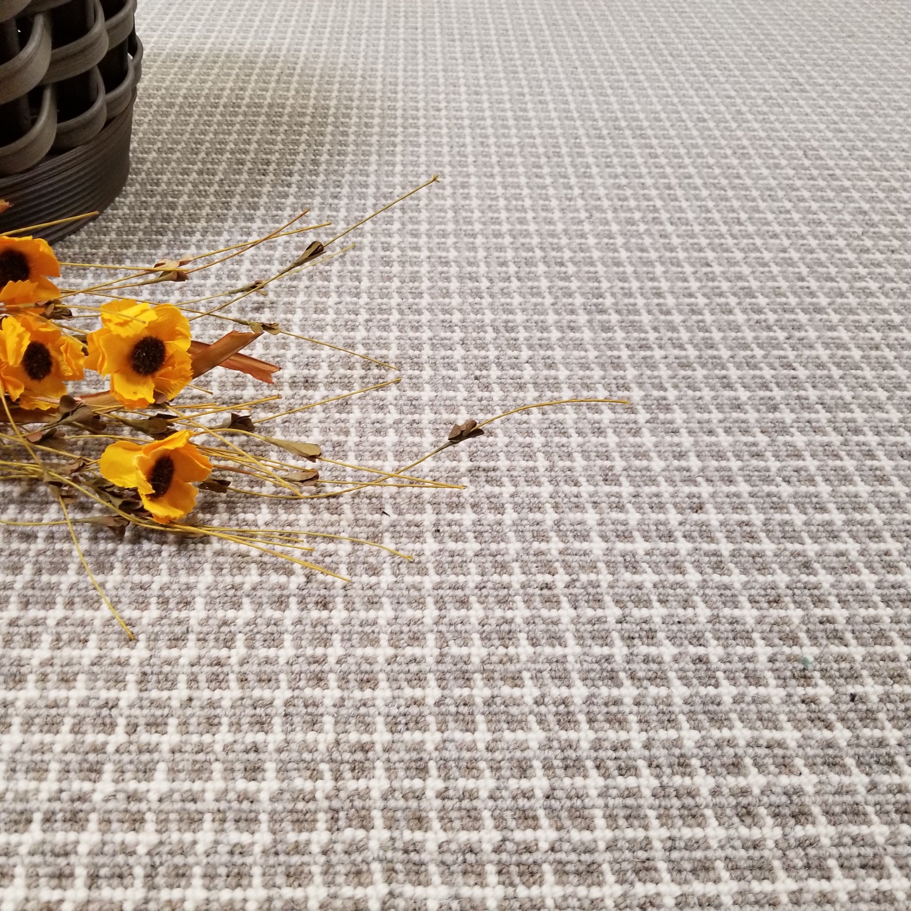 Carpet in a taupe plaid pattern with a small arrangement of yellow flowers and dried elements.