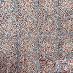 Block printed fabric in a scrolling floral stripe in red on a blue field linen