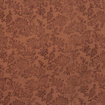Detail of fabric in a paisley print in brown on a burnt orange field.