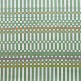 Detail of fabric in a dense irregular check print in green with red, yellow and purple accents on a white field.