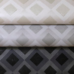 Three rolled pieces of wallpaper in different neutral colorways of a diamond lattice print.