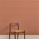 A wallpapered wall in a gridded check pattern in warm pink hues with wooden dining chair. 