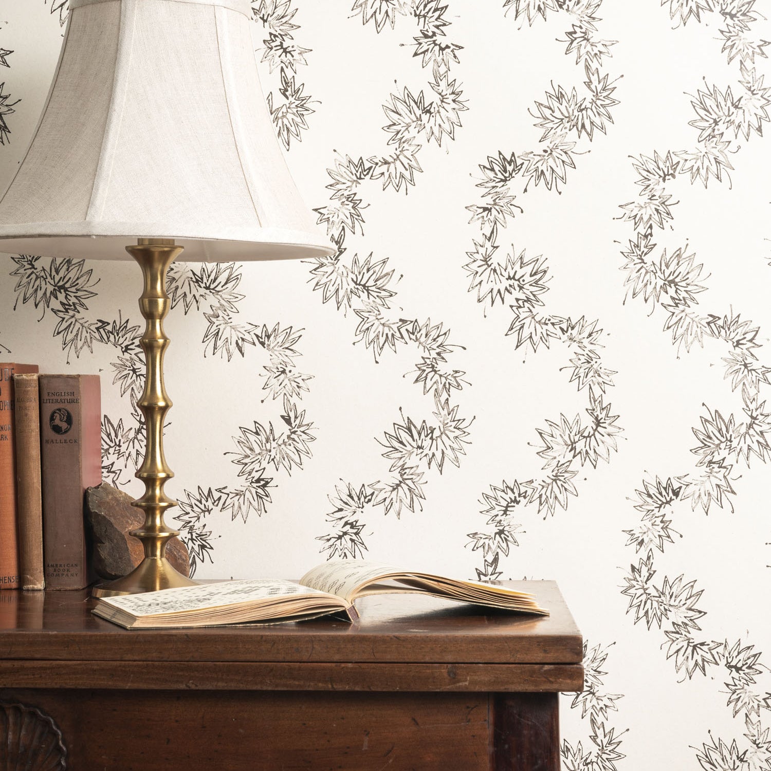 Wooden desk with lamp and books against decorative wallpaper with floral pattern.