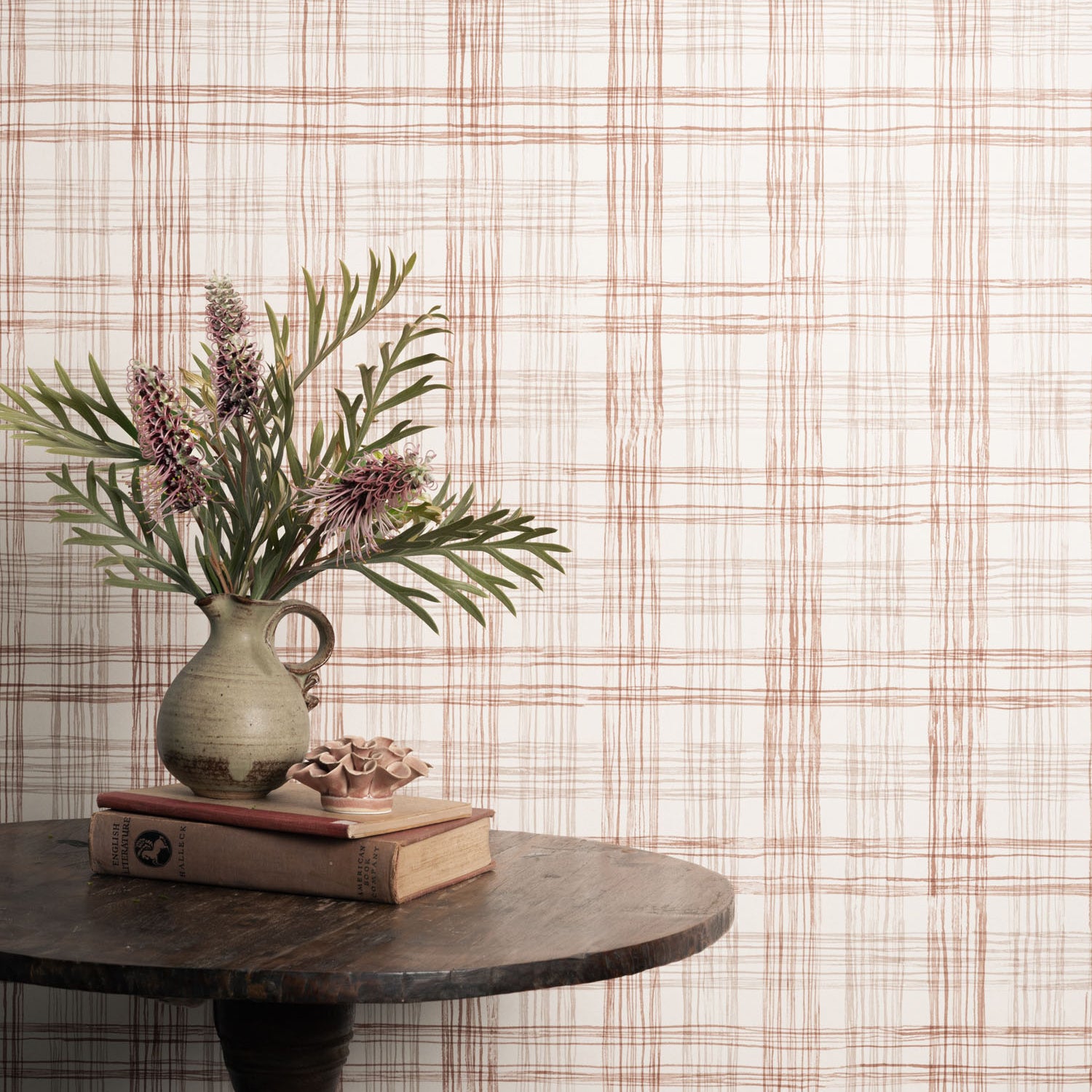 Vase with flowers and books on a table against a plaid wallpaper.