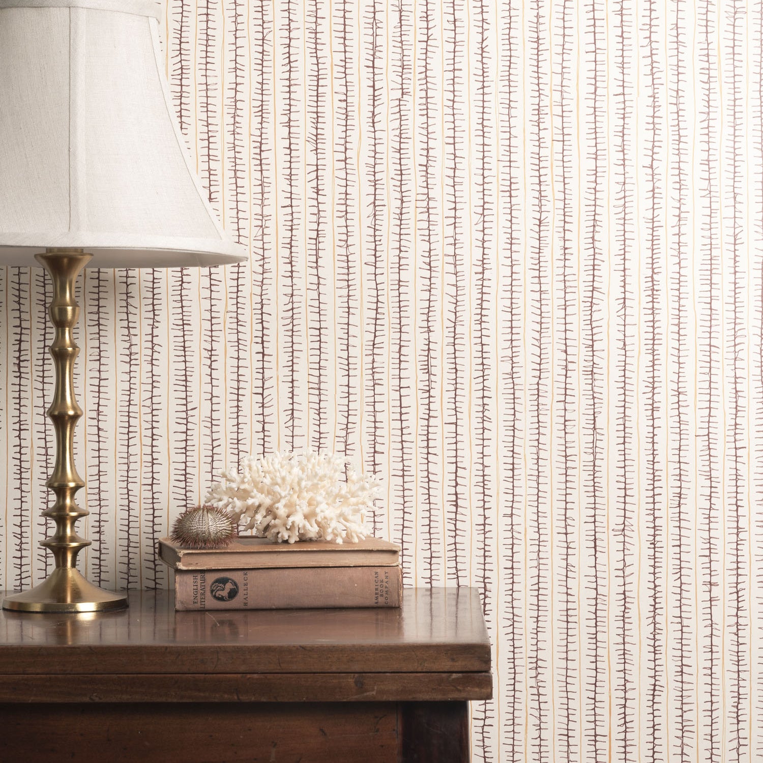 Decorative wallpaper with a subtle pattern, a lamp, and books on a wooden surface.