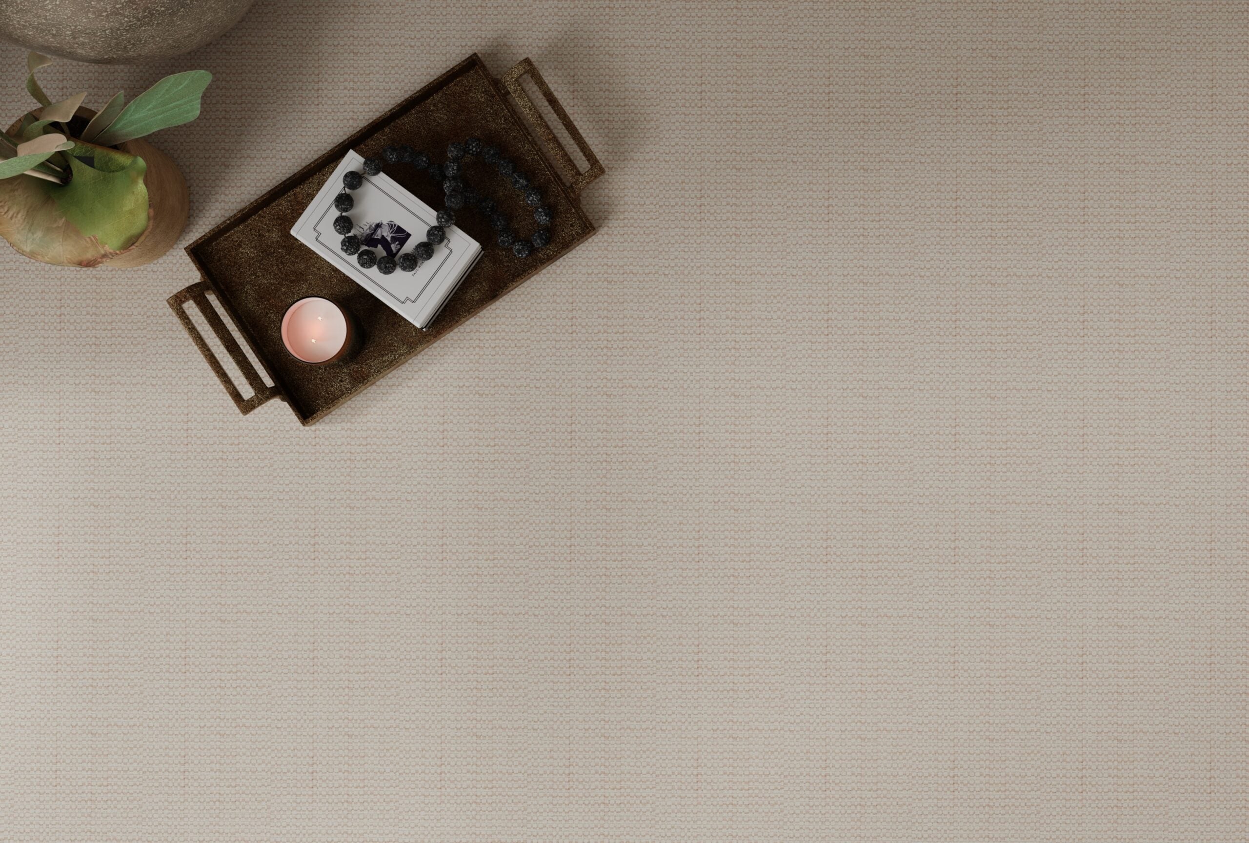 Overhead image of blush broadloom carpet with a metal tray, candle, black beaded necklace and house plant.