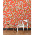 A chair and stool stand in front of a wall papered in large-scale line-drawn flowers in gray ink with red, pink and yellow watercolors, on a red background.