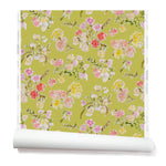 Partially unrolled wallpaper with a pattern of large-scale line-drawn flowers in gray ink with red, pink and yellow watercolors, on a light green background.