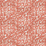 Detail of fabric in a batik splatter print in cream on a coral field.
